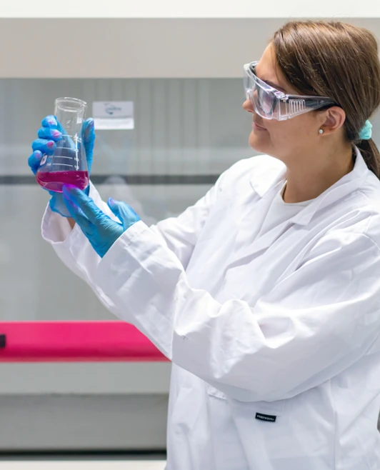 Student in a lab coat studying a beaker of pink liquid under bright lighting in a science lab. Student in a lab coat studying a beaker of pink liquid under bright lighting in a science lab.